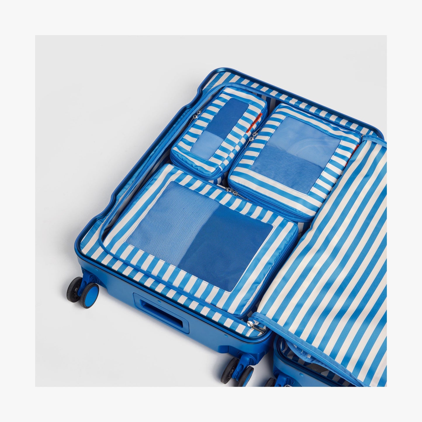 Set of Four / Poplin Stripe Coastal Blue | Poplin Stripe Coastal Blue compressible packing cubes neatly organized inside a Coastal Blue suitcase